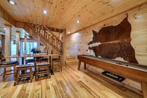 Un interior de madera con una escalera, una zona de bar y un gran cuero de animal en la pared.