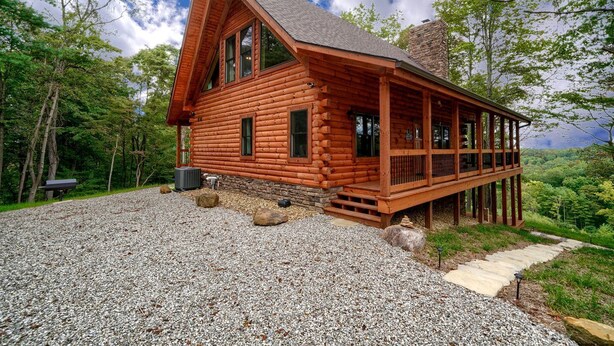 Une cabane en rondins avec un porche, une allée en gravier et une forêt environnante.