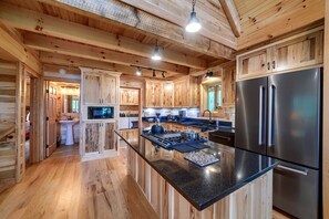 A spacious kitchen with wooden cabinetry, a central island, stainless steel appliances, and a high ceiling with exposed beams.
