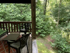 An outdoor deck with a wooden table and chairs, surrounded by lush greenery.