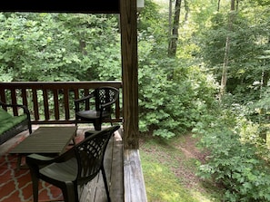 A wooden deck with a table and chairs, surrounded by dense greenery. - Luxury Cabin Rental with Beautiful Water Views near Charlotte, North Carolina (Elkin)