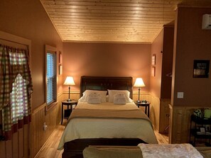 Un dormitorio con techo de madera, una cama con ropa blanca, dos lámparas de noche y una ventana con persianas.