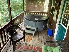 A covered porch with a hot tub, a chair, a small table, and a door. - Luxury Cabin Rental with Beautiful Water Views near Charlotte, North Carolina (Elkin)