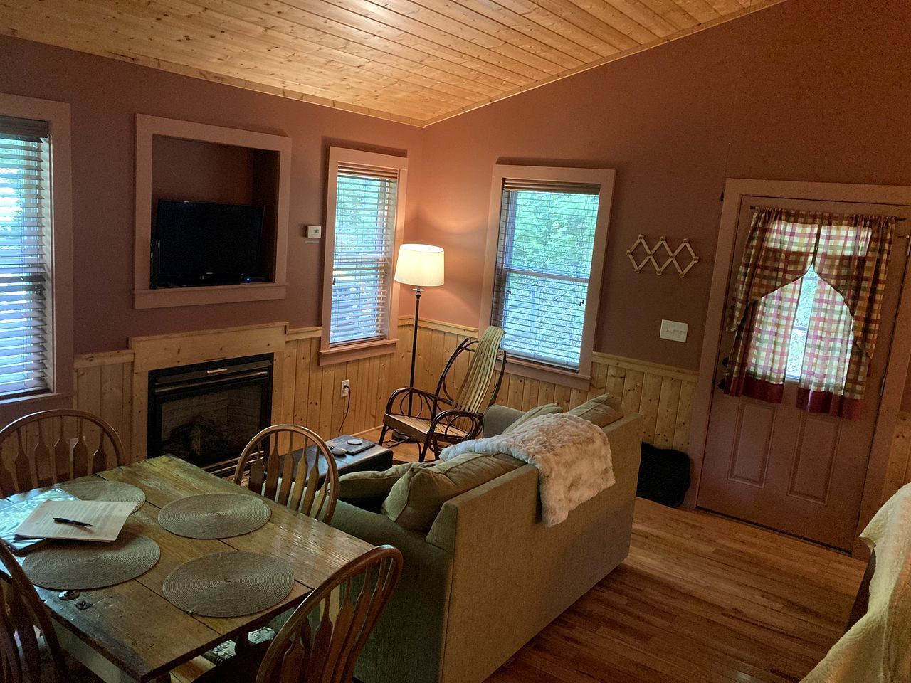 A cozy living room with a fireplace, a television mounted above it, a dining table with chairs, and a sofa.
