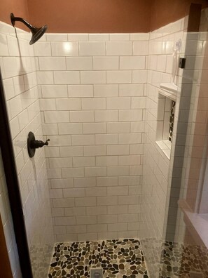 Ducha con azulejos blancos y piso de mosaico de piedra.