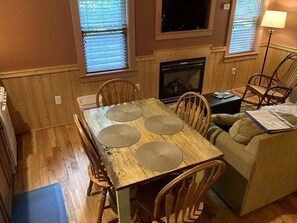 A wooden dining table with four placemats, surrounded by wooden chairs, in a room with wooden walls and a fireplace. - Luxury Cabin Rental with Beautiful Water Views near Charlotte, North Carolina (Elkin)