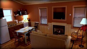 A living room with a fireplace, a television, and a kitchen area. - Luxury Cabin Rental with Beautiful Water Views near Charlotte, North Carolina (Elkin)