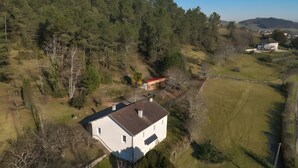 Vista aérea de una casa rodeada de colinas boscosas, con un patio cercado y un panel solar en el techo.