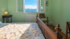 Un dormitorio con cama, ventana, silla y radiador.
