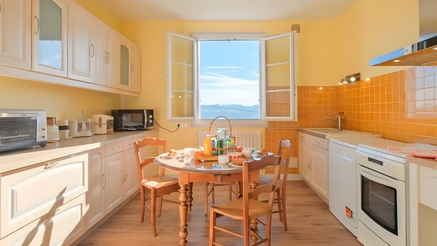 Una cocina con mesa, sillas, armarios, microondas y ventana con vista despejada.