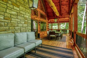 A log cabin with a stone wall, a sofa, a dining table with chairs, and a wooden deck.