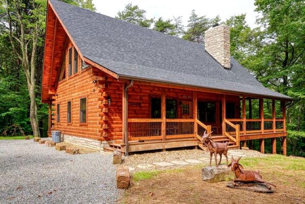 A log cabin with a porch, a chimney, and two deer statues.