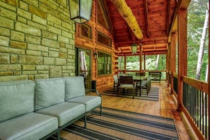 A log cabin with a stone wall, a sofa, a dining table with chairs, and a wooden deck.