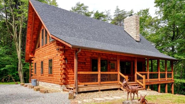 A log cabin with a porch, a chimney, and two deer statues. - Hocking Hills Park Getaway for Family Adventures in Logan, Ohio (Logan)