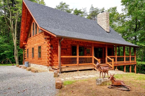 A log cabin with a porch, a chimney, and two deer statues.