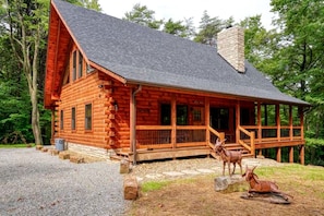 A log cabin with a porch, a chimney, and two deer statues.