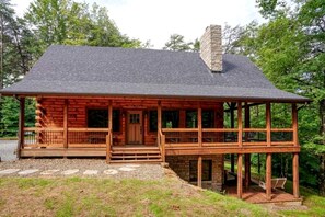 A log cabin with a porch, a chimney, and a stone foundation.