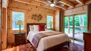 A wooden cabin bedroom with a bed, two nightstands, a ceiling fan, and large windows. - Hocking Hills Park Getaway for Family Adventures in Logan, Ohio (Logan)