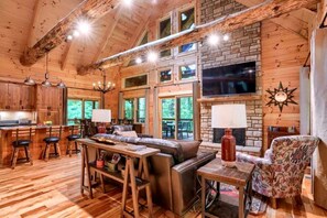 A cabin interior with a wooden interior, a fireplace, a television, and a dining area.