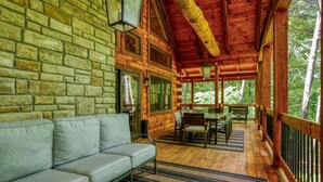 A log cabin with a stone wall, a sofa, a dining table with chairs, and a wooden deck. - Hocking Hills Park Getaway for Family Adventures in Logan, Ohio (Logan)