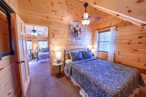 A wooden cabin bedroom with a bed, bedside tables, a ceiling fan, and a window.