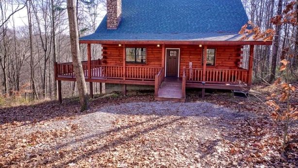 A log cabin with a porch, a chimney, and a door.