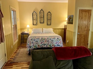 A bedroom with a bed, a nightstand, a lamp, a door, and a window with blinds.