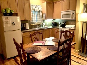 A compact kitchen with wooden cabinets, a microwave, a refrigerator, and a dining table with chairs. - Rustic Cabin on 28-Acre Property in the Foothills of the Blue Ridge Mountains (Elkin)