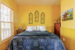 A hotel room with a bed, a nightstand, a lamp, a dresser, and a painting on the wall. - Rustic Cabin on 28-Acre Property in the Foothills of the Blue Ridge Mountains (Elkin)