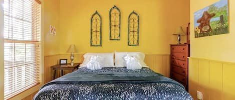 Une chambre d’hôtel avec un lit, une table de chevet, une lampe, une commode et un tableau au mur.