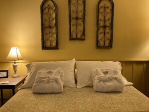 A hotel room with a bed, two pillows, two towels, a nightstand with a lamp, and three wall-mounted decorative panels. - Rustic Cabin on 28-Acre Property in the Foothills of the Blue Ridge Mountains (Elkin)