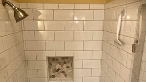 A shower with white tiles, a small pebble accent, and a showerhead. - Rustic Cabin on 28-Acre Property in the Foothills of the Blue Ridge Mountains (Elkin)