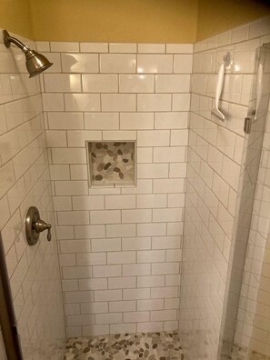 A shower with white tiles, a small pebble accent, and a showerhead. - Rustic Cabin on 28-Acre Property in the Foothills of the Blue Ridge Mountains (Elkin)
