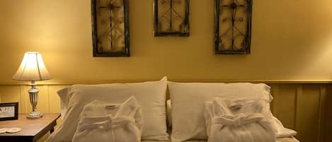 A hotel room with a bed, two pillows, two towels, a nightstand with a lamp, and three wall-mounted decorative panels.