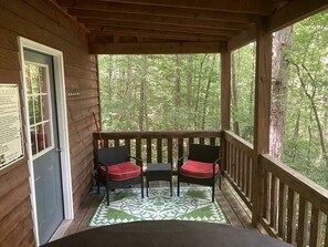 Une véranda en bois avec deux chaises et une table, une porte et une vue sur une forêt.