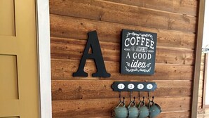 Eine Holzwand mit einem Schild zum Thema Kaffee, einer Kaffeemaschine und Tassen auf einem Tisch.