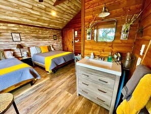 A cabin-style room with two beds, a wooden ceiling, a sink, and a mirror.