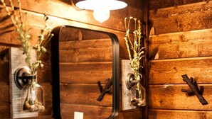 A bathroom with a wooden wall, a white sink, a mirror, a light fixture, and a small plant.