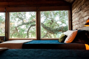 A room with a large window, a bed with a blue bedspread, and a wooden wall. - Tranquil Dripping Springs Vacation Rental Ideal for Texas Getaways (Dripping Springs)