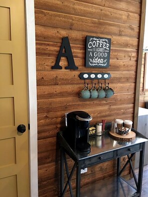 Un mur en bois orné d’une enseigne sur le thème du café, une machine à café et des tasses posées sur une table.