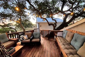 Eine Holzterrasse mit Sitzgelegenheit, einem Baum und Lichterketten.