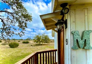 A wooden porch with a railing, a lamp, and a large 'M' sign on the wall. - Tranquil Dripping Springs Vacation Rental Ideal for Texas Getaways (Dripping Springs)