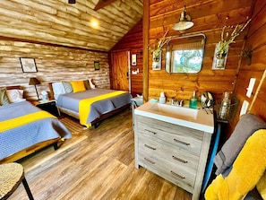 A cabin-style room with two beds, a wooden ceiling, a sink, and a mirror.