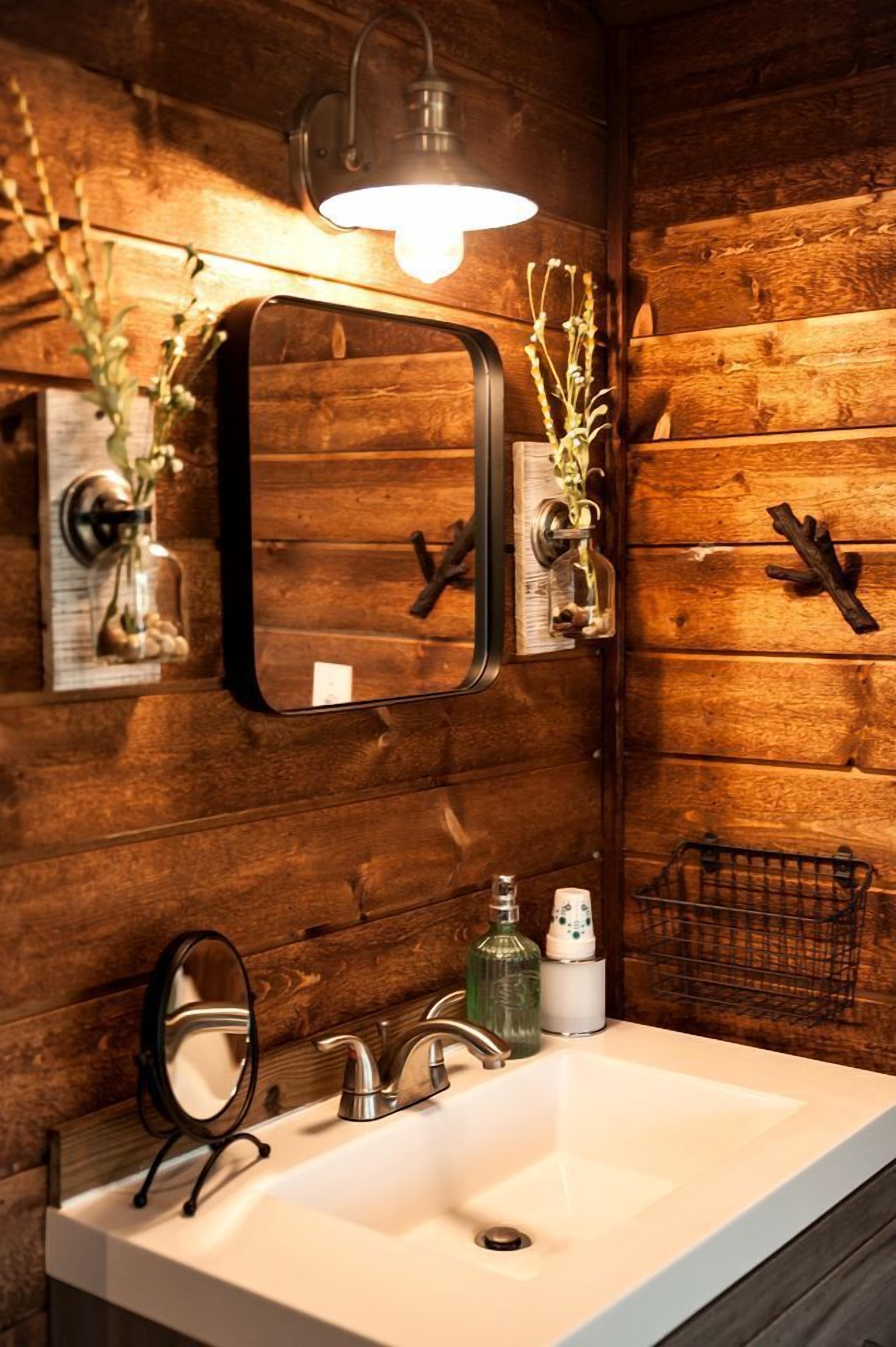 A bathroom with a wooden wall, a white sink, a mirror, a light fixture, and a small plant.