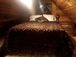Un lit recouvert d’une couvre-lit à motifs, dans une pièce aux murs en bois et dotée d’une fenêtre.