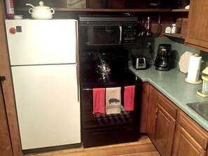 A compact kitchen with a refrigerator, oven, microwave, and coffee maker.
