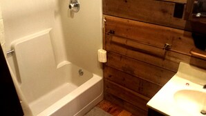 A bathroom with a bathtub, toilet, wooden wall paneling, and a sink. - Cozy Vacation Rental with High-Speed Wi-Fi near Seven Springs, Pennsylvania (Champion)