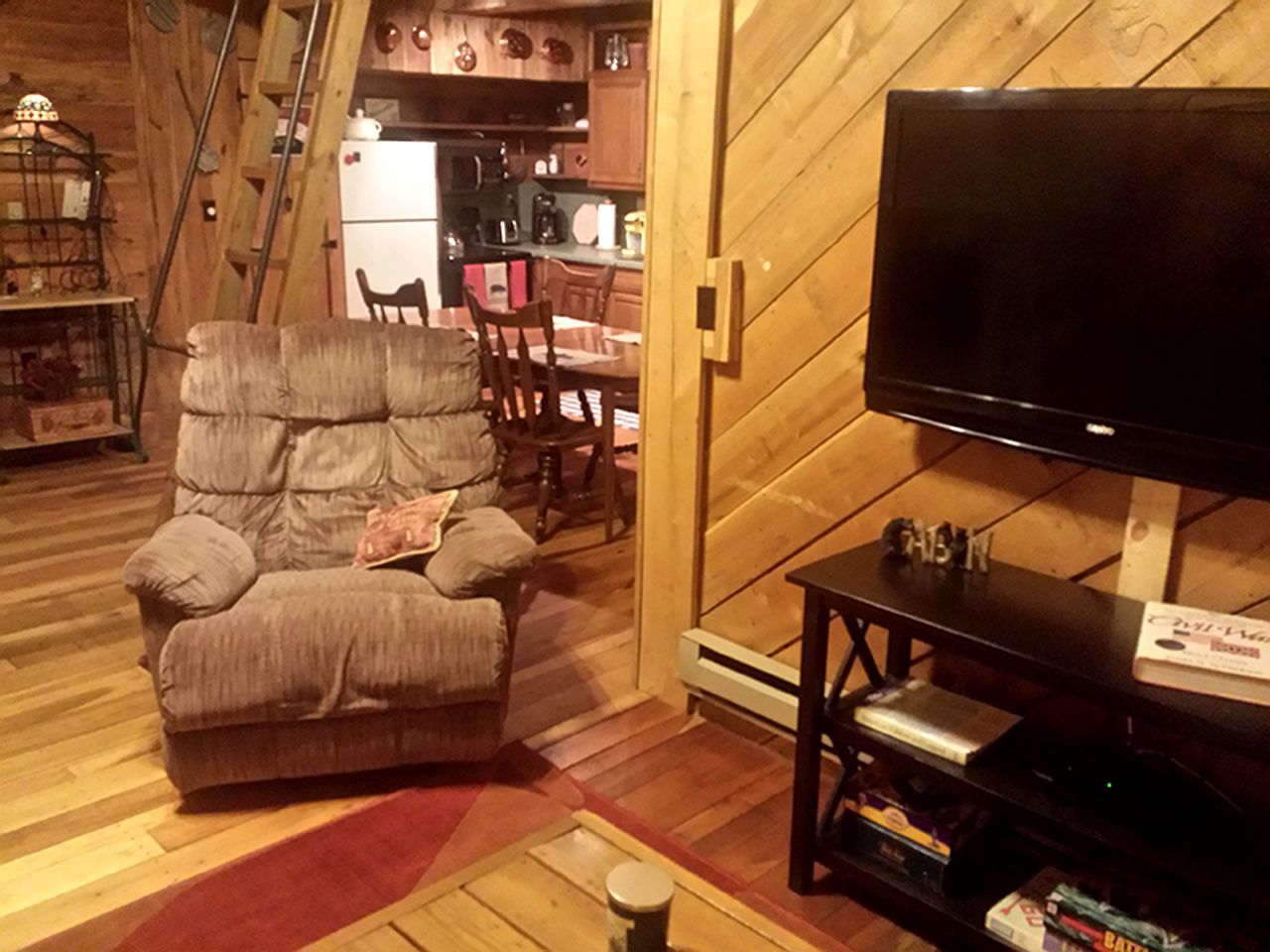 A cozy living room with a large flat-screen TV, a comfortable armchair, and a wooden dining table.