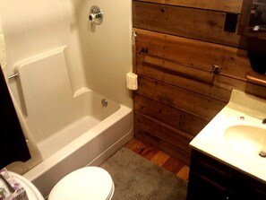 A bathroom with a bathtub, toilet, wooden wall paneling, and a sink. - Cozy Vacation Rental with High-Speed Wi-Fi near Seven Springs, Pennsylvania (Champion)