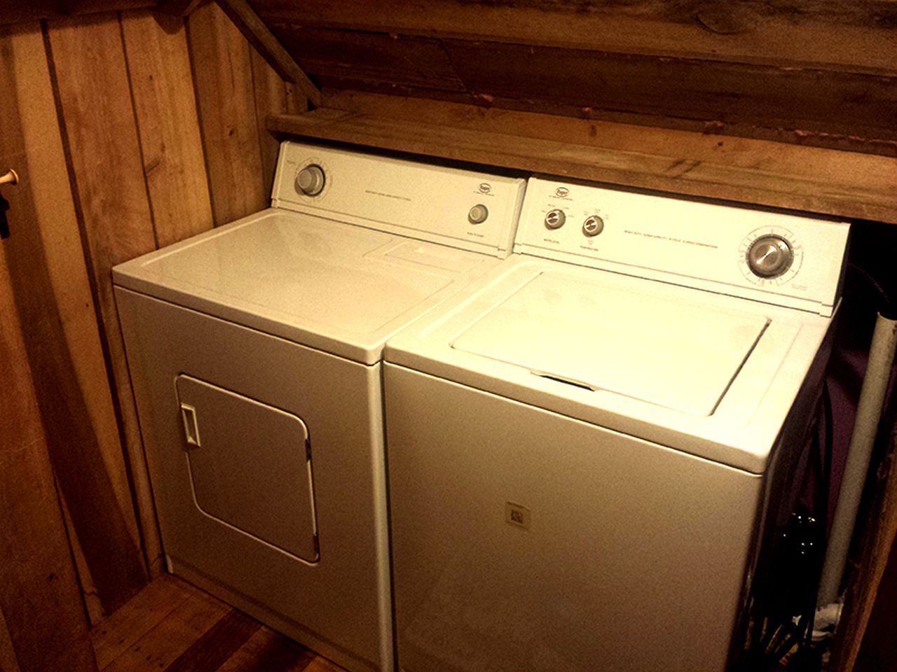 A laundry room with two stacked washers and dryers, wooden walls, and a metal door.